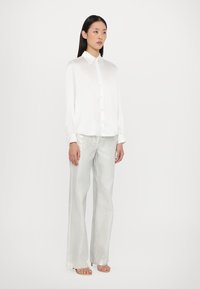 Chemise blanche à manches longues avec un col classique, associée à un pantalon large en argent clair brillant. Tissu lisse et fluide.
