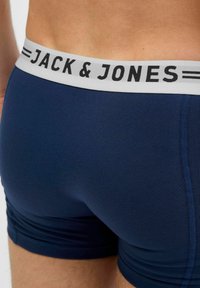 Navy zils bokseris ar gludu audumu, ar pelēku jostu, kurā ir melna "JACK & JONES" emblēma un kontrastējoši stitching sīki elementi.