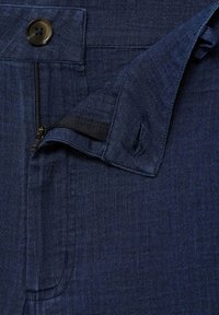 Mornarsko modri kavbojke imajo gladko teksturo, viden gumb in zadrgo. Pas ima ojačan del za večjo trpežnost.