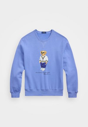 Sweat-shirt bleu clair à manches longues et col rond avec un motif représentant un ours portant des lunettes de soleil, un pull blanc et un pantalon bleu marine.