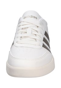 Vita Adidas-sneakers med en slät läderöverdel, som har tre mörkgrå ränder, rund tå och platt krämfärgad gummisula.