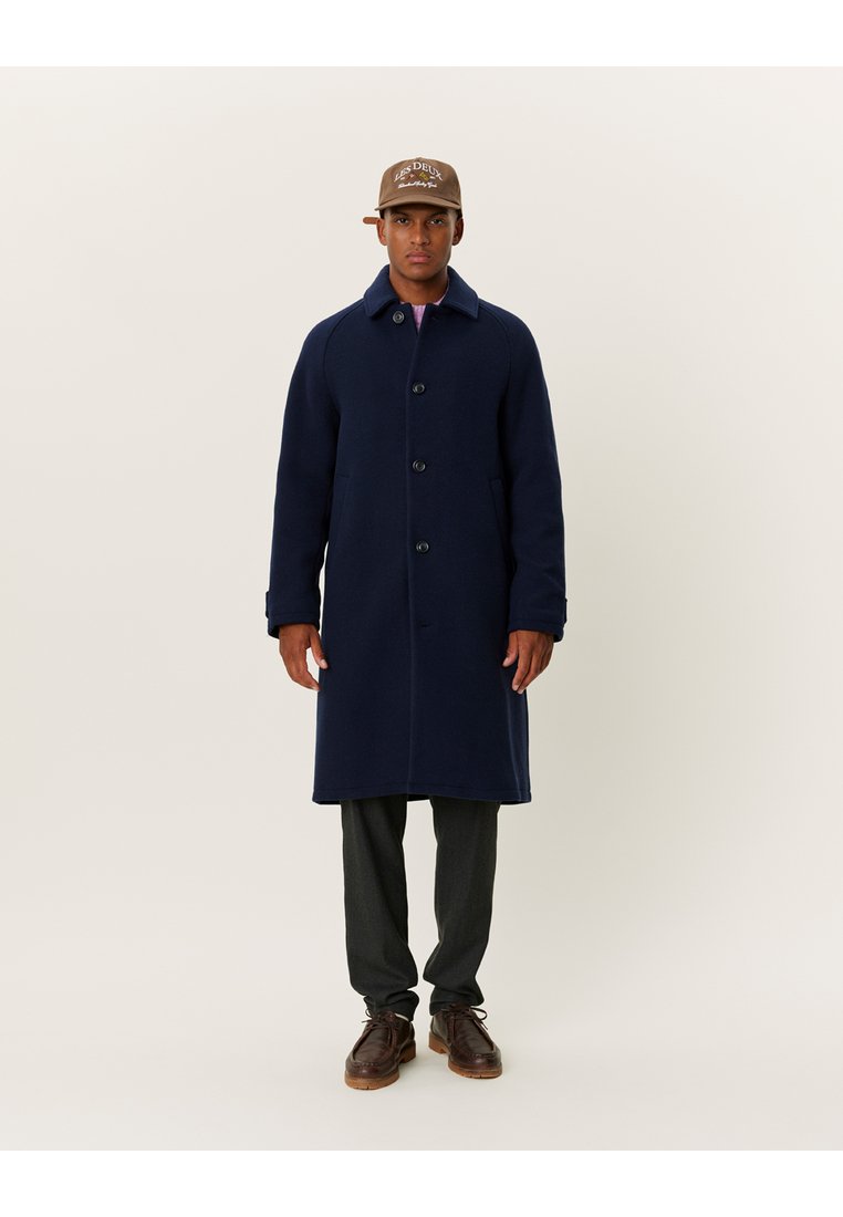 Ναυτικό παλτό από μαλλί με ίσια γραμμή, μπροστινές κουμπότρυπες και πλαϊνές τσέπες. Συνδυάζεται με σκούρες παντελόνες και καφέ δερμάτινα παπούτσια.