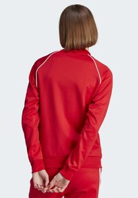 Röd sweatshirt med hög krage och långa ärmar, med vit kantning längs axelsömmarna och en mjuk yta.