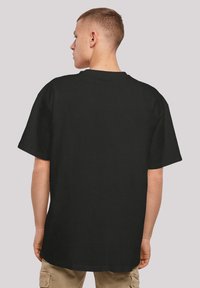 Schwarzes T-Shirt mit kurzen Ärmeln, aus Baumwolle, mit Rundhalsausschnitt und lässiger Passform, von hinten betrachtet. Glatte Textur und keine sichtbaren Muster.