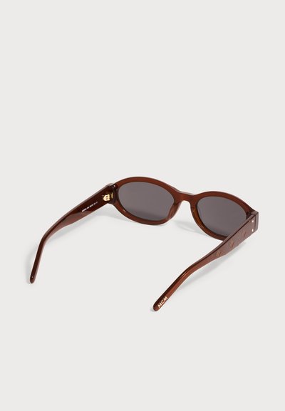 Lunettes de soleil ovales marron avec verres foncés, branches larges avec motifs en relief et logo "MCM" à l'extrémité de la branche droite.