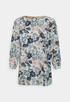 Blouse florale avec un fond bleu clair, des manches longues, un col rond et un mélange de motifs floraux roses, marine et verts.