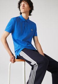 Granatowa koszulka polo z kołnierzykiem i trzema guzikami, zestawiona z granatowymi dresami z białymi pasami po bokach. Prosty design i miękka tkanina.