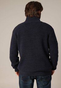 Pull en maille texturée bleu marine avec un col montant et des poignets côtelés, vu de l'arrière. Motif en nid d'abeille, coupe décontractée.