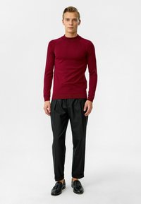 Chemise bordeaux à manches longues avec un col côtelé, associée à un pantalon noir plissé et des mocassins noirs. Texture de tissu lisse, design ajusté.