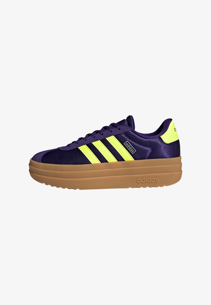 Paarse Adidas sneaker met neongele strepen en hieltab, dikke lichtbruine plateaus zool, zijkantlogo en vetersluiting aan de voorkant.