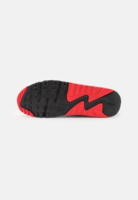 Semelle de chaussure avec une semelle extérieure en caoutchouc noir et rouge présentant des motifs carrés et linéaires, une rainure en zigzag et un logo "NIKE" près du centre.