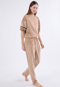 Beige loungewear set gemaakt van ribbelstof; bevat een cropped top met wijde mouwen en broek met trekkoord en zijzakken.