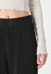 Pantalons plissés noirs avec taille élastique, associés à un haut blanc court en ribbe avec des bords festonnés.