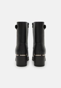 Bottines en cuir noir avec une finition texturée, dotées d'un talon bloc moyen et d'un accent métallique doré autour de la base du talon.