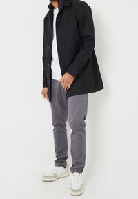 Veste noire à boutons, pantalon gris et baskets blanches. La veste a une coupe droite et un col, tandis que le pantalon est fuselé.