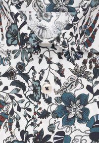 Camicia bianca con motivo floreale blu e nero, con bottone bianco e un colletto visibile al centro superiore.