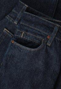 Jeans de mezclilla en azul oscuro, con una textura suave, diseño estándar de cinco bolsillos y costuras claras contrastantes a lo largo de las costuras.