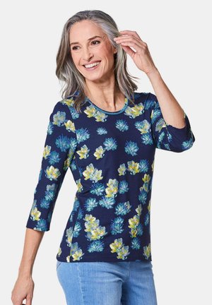 Navy top met een bloemmotief, driekwart mouwen, ronde hals en blauwe afwerking, gemaakt van zachte stof met een lichte glans.