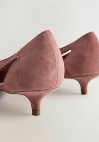 Par af støvede rosa ruskind kitten heels med lukkede tåspidser og lave stiletter på en neutral baggrund.
