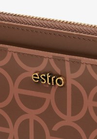 Brązowy portfel z geometrycznym wzorem, złotymi elementami i zapięciem na zamek błyskawiczny. Logo "Estro" wyeksponowane w złotym kolorze na przodzie.