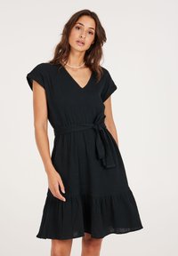 Zwarte jurk met korte mouwen en V-hals, met een cinched taille en strikdetail. Beschikt over een uitlopende rok met een gelaagde ruches zoom en een gestructureerde stof.