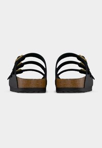 Ζευγάρι μαύρων σανδαλιών με τρεις ρυθμιζόμενους ιμάντες και πέλματα από φελλό, σε προοπτική από πίσω, σε μονόχρωμο γκρι φόντο.