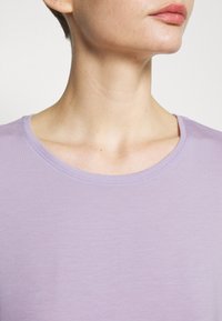 Svetle fialová košile s krátkým rukávem a kulatým výstřihem. Tkanina vypadá jemně a hladce s mírným leskem. Minimalistický design.