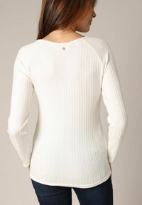 Pull blanc à manches longues et côtes, fabriqué dans une texture tricotée, avec un col rond et une petite décoration à l'arrière.