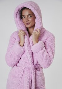Rosa fluffig badrock med huva, stora manschetter, knytband och två framfickor. Mjuk, strukturerad material genom hela.
