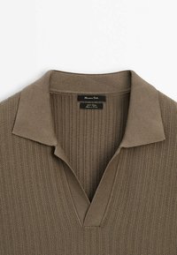 Polo shirt tricoté marron avec une texture côtelée, comportant un col classique et une petite étiquette au cou.