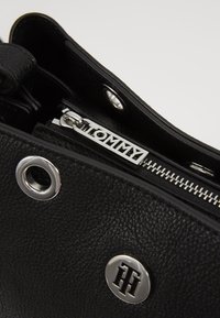 Musta nahkakäekott, millel on tekstureeritud pind, hõbedased detailid, nähtav lukuga brändi silt ja ümmargused metallaktsendid.