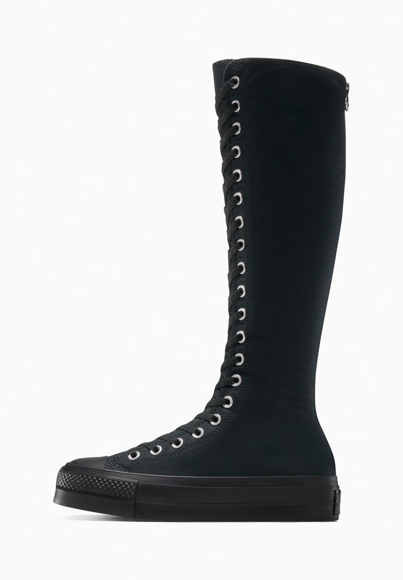 Hoher schwarzer Leinensneaker mit Schnürung, dicker Gummisohle und Reißverschluss an der Ferse, von der Außenseite auf weißem Hintergrund betrachtet.