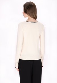 Maglione avorio con maniche lunghe, scollatura rotonda e bordatura nera intorno al collo e alle maniche. Texture a maglia liscia.