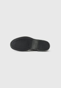 Semelle de chaussure en caoutchouc noir avec des rainures horizontales et verticales pour une meilleure adhérence. Présente une section renforcée au niveau du talon, marquée "GEOX."