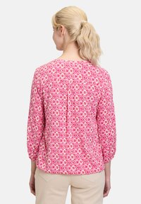 Rosa gemusterte Bluse mit einem diamant- und blumenartigen Design, Dreiviertelärmel und einem Rundhalsausschnitt. Weicher Stoff mit lockerer Passform.