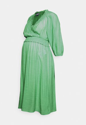 Vestido de maternidade verde feito de tecido leve. Apresenta um decote em V, cintura franzida e mangas baloon de três quartos.