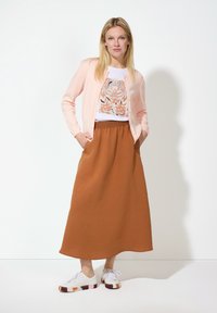 Hellfarbener Cardigan über einem weißen T-Shirt mit einem braunen Blumenmuster. Fließender brauner Maxiskirt und weiße Sneakers mit mehrfarbigen Akzenten.