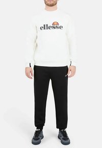 Weißer Sweatshirt mit "ellesse" Logo, schwarze Hose und dunkle Sneakers. Glatte Textur und lockere Passform. Schlichtes Design mit Logo-Akzenten.