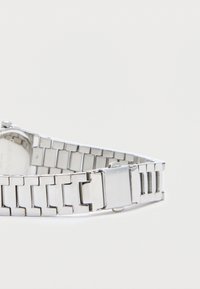 Montre-bracelet en métal argenté avec un design à bracelet maillons, présentant une finition brillante et une fermeture à fermoir, avec un cadran partiellement visible.