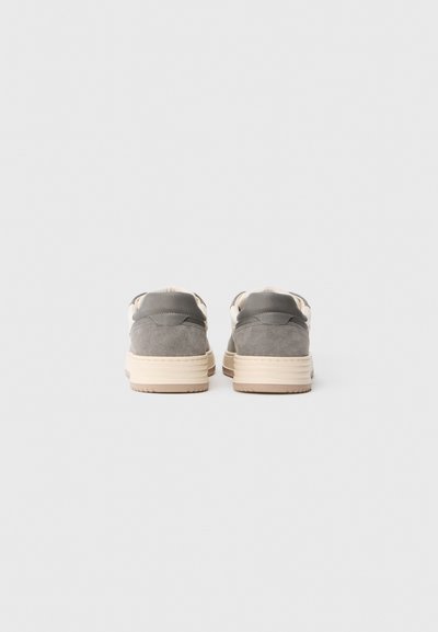 Szare zamszowe sneakersy z beżowymi gumowymi podeszwami. Posiadają gładki skórzany akcent przy pięcie oraz niskoprofilowy, zaokrąglony design.