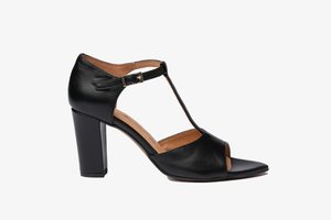 Zapato de tacón alto de cuero negro con diseño de tira en T, punta abierta y tacón grueso. Cuenta con una hebilla en tono dorado y plantilla texturizada.