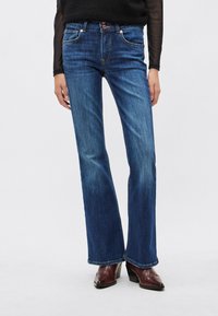 Siniset denim-farkut, levenevät lahkeista, keskikorkea vyötärö, sileä pinta, hillitty haalistuminen, viisipokainen muotoilu ja kuparinväriset metalliosat, yhdistetty ruskeisiin korkokenkiin.