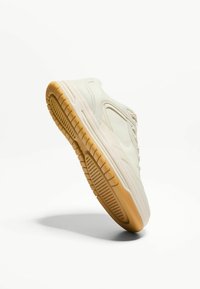 Beżowe sneakersy z gładką cholewką, zaokrąglonym noskiem i teksturowaną gumową podeszwą. Posiada minimalistyczny design i subtelne detale przeszycia.