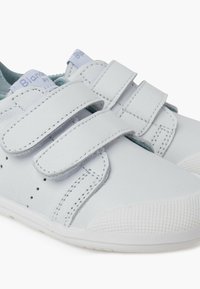Baltos odinės sportbačiai su Velcro dirželiais, perforuotomis detalėmis ir tekstūruotu guminio pado. Iškloti šviesiai mėlynu audiniu komfortui.