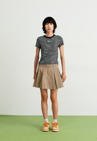 Camisa de manga curta às riscas pretas e brancas, saia bege com pregas, ténis laranja e meias cinzentas claras. Design simples, roupa casual.