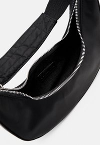 Borsa a tracolla nera in nylon con spallaccio trapuntato, chiusura superiore con zip e interno testurizzato con un'etichetta logo discreta.