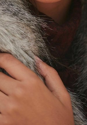 Faux fur collar in gray tones, featuring long, soft fibers. Hand with medium skin tone rests on the collar. Rich maroon fabric underneath.