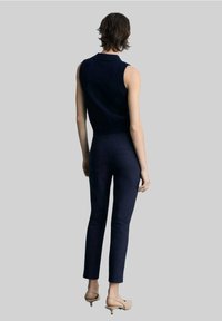 Haut sans manches en maille marine associé à un pantalon slim marine. Texture lisse, coutures minimales et design épuré. Des talons beiges complètent le look.