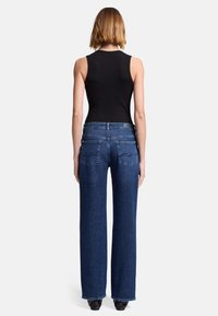 Dżinsowe spodnie o szerokich nogawkach w ciemnoniebieskim kolorze z wysokim stanem, z dwoma tylnymi kieszeniami i subtelnymi detalami w szwach. Połączone z czarnym topem bez rękawów.