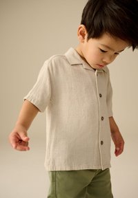 Licht beige linnen overhemd met korte mouwen en een gestructureerde afwerking, voorzien van een reverskraag en donkere knopen, gecombineerd met groene broek.